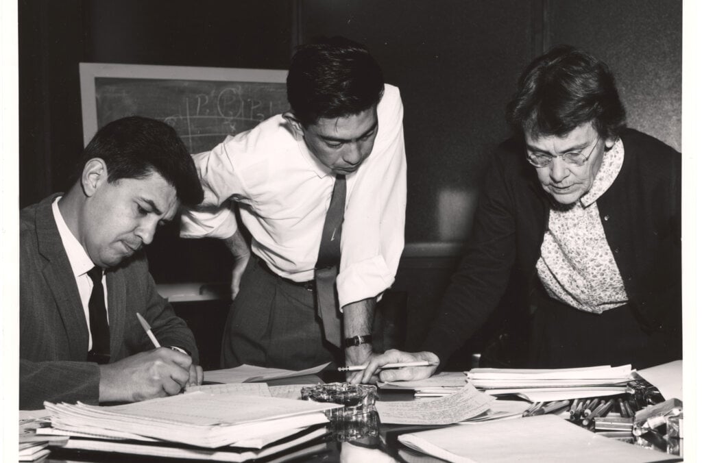 Two men and a woman looking at papers on a desk