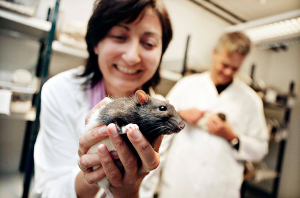 A woman with a mouse. A amn is standing in the background