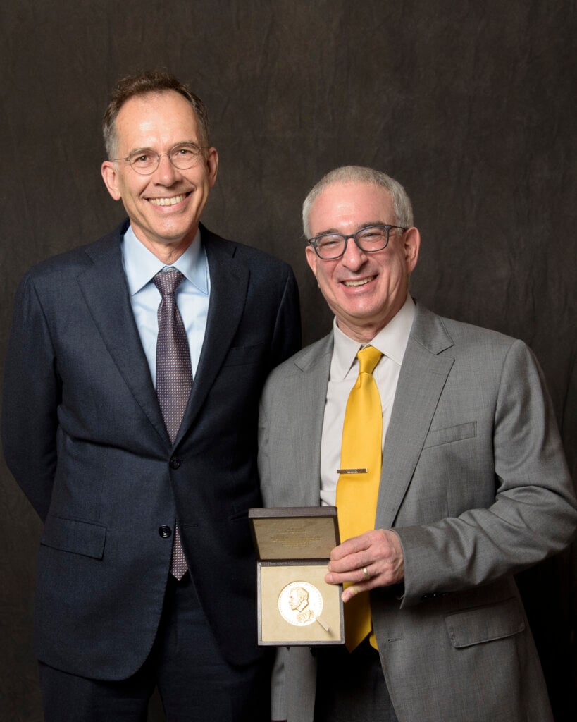 Guido Imbens and Joshua Angrist, in suits, pose with Angrist's Nobel Prize medal.