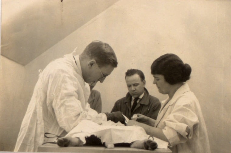 Original black and white photograph showing Banting, assisted by Sadie Gairns, performing surgery on a dog. Unidentified man in background.