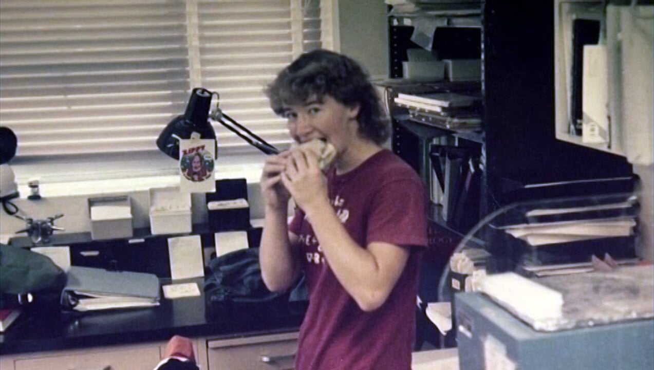 A woman in a laboratory eating a sandwich
